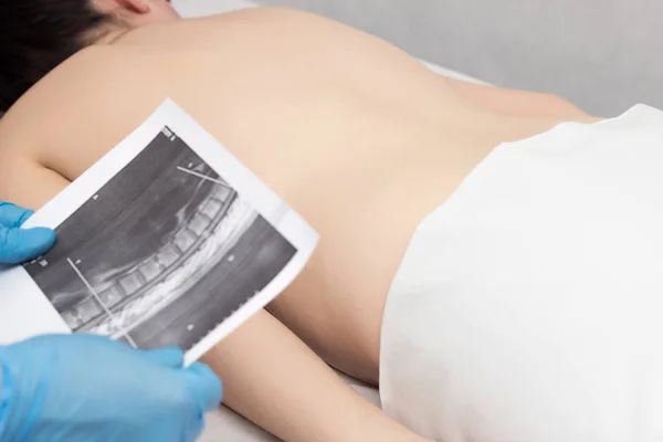 Doctor holds an MRI shot on the back of a girl who has a backache, back problems, neurology, inflammation — Stock Image Doctor holds an MRI shot on the back of a girl who has a backache, back problems, neurology, inflammation Stock Photo