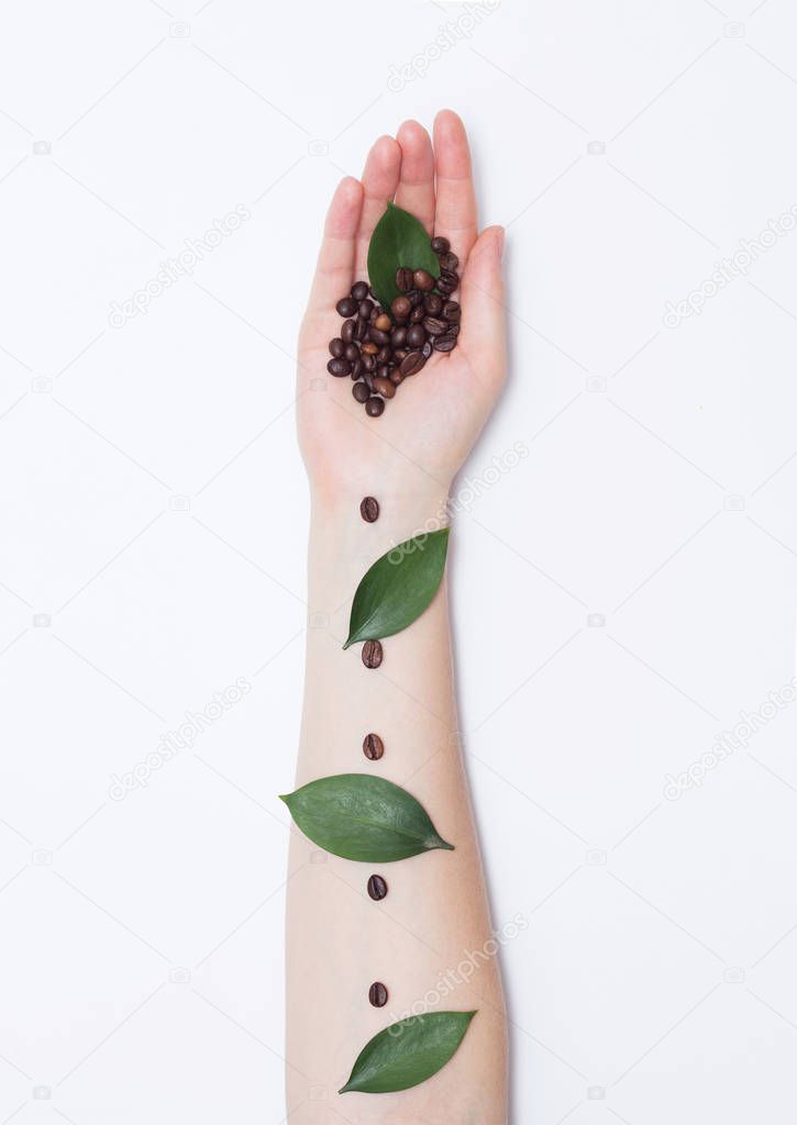 Female hand with coffee grains in the palm and petals on a white background, fashionable handmade art, cosmetic