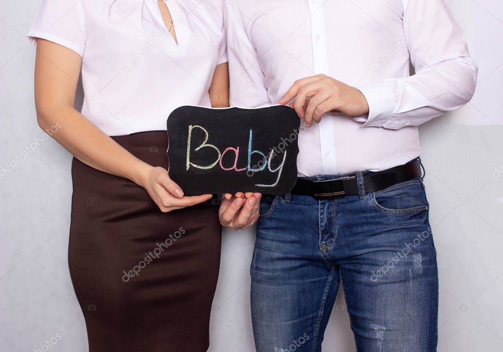 A man and a woman stand with a sign on which the baby is written, problems with the conception of children, male and female infertility