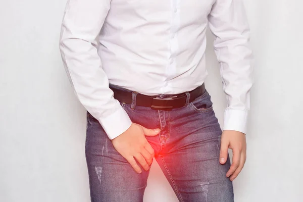 Un hombre sobre un fondo blanco con una camisa blanca aferrándose a su ingle tiene dolor y varicocele del cordón espermático, un problema, venas varicosas — Foto de Stock