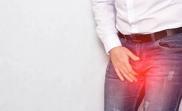 Um homem com uma camisa branca segurando sua virilha com uma infecção e prostatite, urologia, espaço de cópia, inflamação — Fotografia de Stock