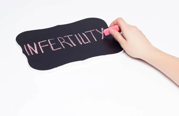 Flickan skriver med krita på svarta tavlan ordet infertilitet, närbild, kopia utrymme, hand, vit bakgrund — Stockfoto