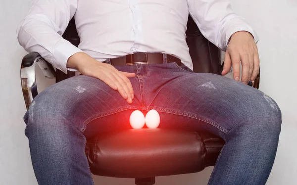 Ένας άντρας με λευκό πουκάμισο κάθεται σε μια καρέκλα με μια κύστη της επιδιδυμίδας του όσχεου, η ορόρτιδα και η φλεγμονή, ο πόνος — Φωτογραφία Αρχείου