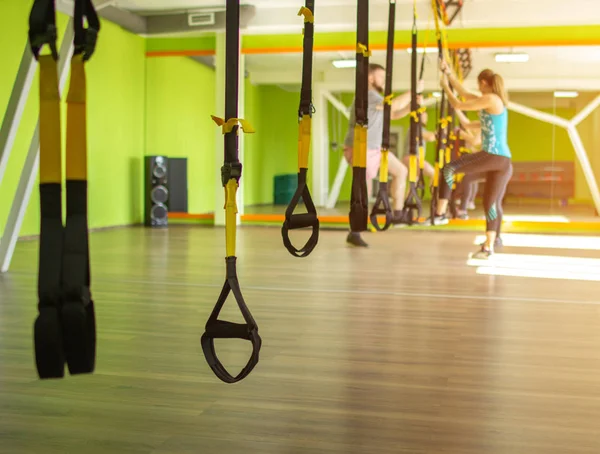 Cours de groupe avec un entraîneur et entraînement sur la boucle de sport TRX dans le nouveau complexe de fitness moderne, espace de copie, personnes — Photo