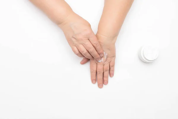 一位老年妇女用保护霜涂抹双手，用于抚平皱纹和恢复脱水、全面的护手霜、白色背景、复制空间、水脂膜 — 图库照片