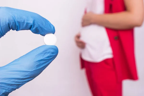 Ο γιατρός κρατά ένα χάπι με τη μορφή ενός συγκροτήματος βιταμινών και φυλλικού οξέος στο φόντο μιας εγκύου κοριτσιού, έλλειψης βιταμινών και ασβεστίου κατά τη διάρκεια της εγκυμοσύνης — Φωτογραφία Αρχείου