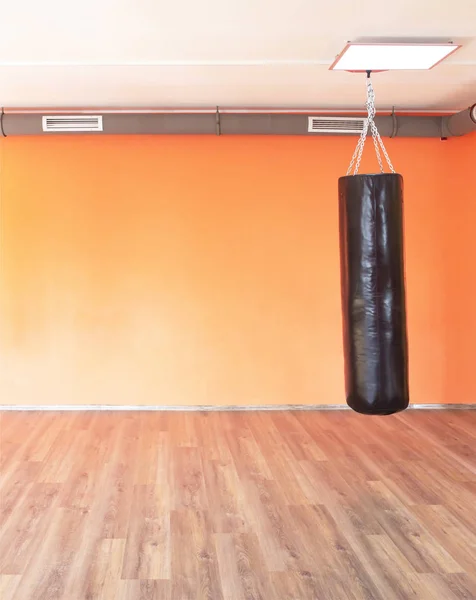Boxing modern punching bag on the background of the orange wall in the new modern gym, copy space