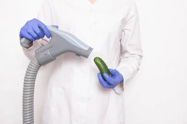 Ο γιατρός κρατά ένα αγγούρι κοντά στην ηλεκτρική σκούπα σε λευκό φόντο, την έννοια της αύξησης του πέους σε άνδρες με αντλία κενού, αυξάνοντας το μήκος του αρσενικού οργάνου — Φωτογραφία Αρχείου