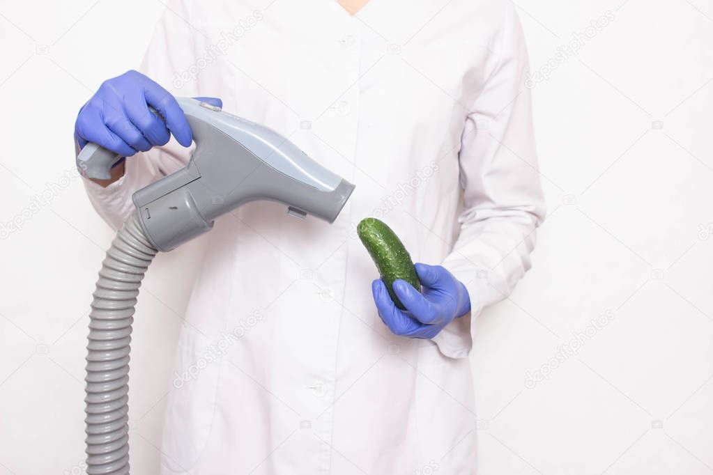 Doctor holds a cucumber near the vacuum cleaner on a white background, the concept of increasing penis in men with a vacuum pump, increasing the length of the male organ