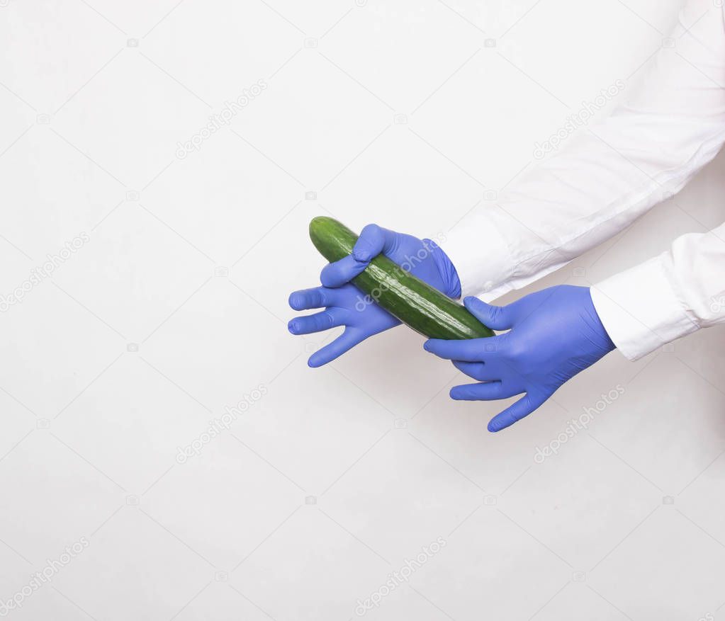 The doctor in medical gloves holds a cucumber in his hands, the concept of increasing the penis with the help of massage techniques and techniques, white background, copy space