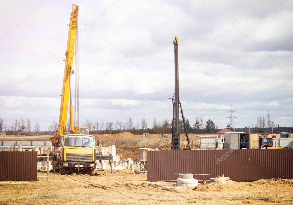 Erection of a foundation for a multi-storey residential building, a truck crane lifts roadhead piles, piling machinery, diesel hammer, special equipment