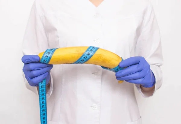 O médico segura banana na mão com fita métrica. Conceito de aumento do pênis masculino e operação, aumento do órgão masculino — Fotografia de Stock