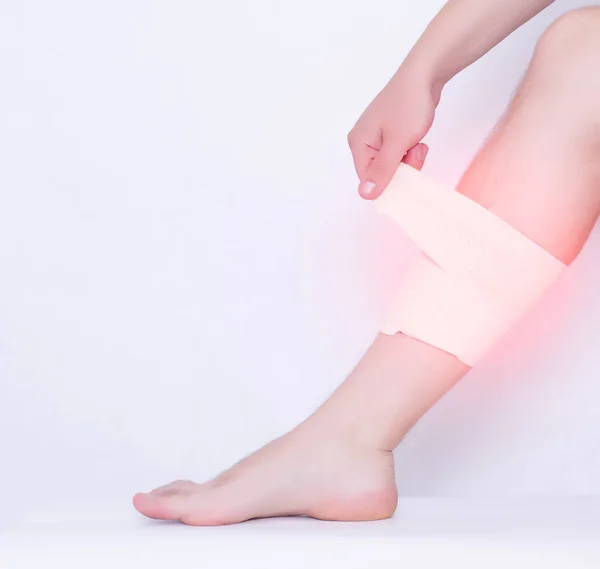 Um homem puxa uma bandagem elástica em uma entorse do músculo gastrocnêmio em que dor e inflamação, entorse da perna, fundo branco, espaço de cópia — Fotografia de Stock