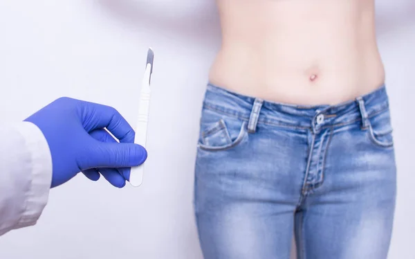 The doctor holds a scalpel on the background of the abdomen of the girl. The concept of surgery for inflammation of appendicitis, medical