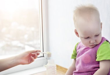 Anne, çocukların kötü beslenmesi, sindirim sorunları, kopya alanı kavramını başını kapatan küçük çocuğuna yemekle bir kaşık uzatır.
