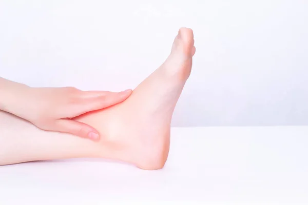 A menina se agarra à articulação do tornozelo dolorido em que a inflamação tende e alonga o aparelho ligamentar, fundo médico, branco, espaço de cópia — Fotografia de Stock