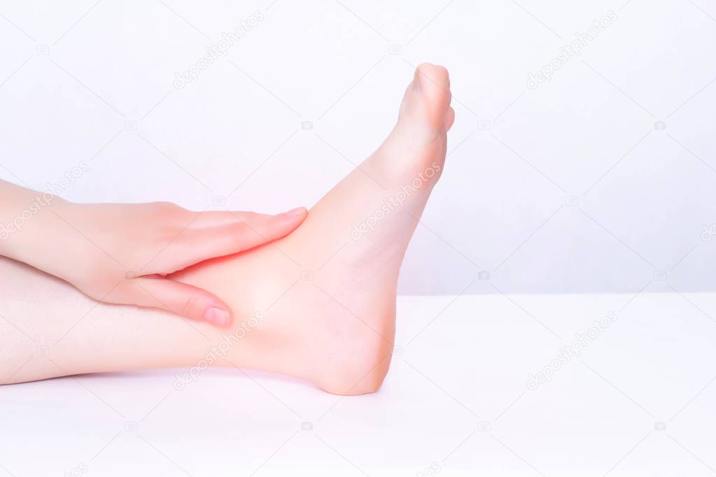 The girl holds on to the sore ankle joint in which the inflammation tends and stretches the ligamentous apparatus, medical, white background, copy space