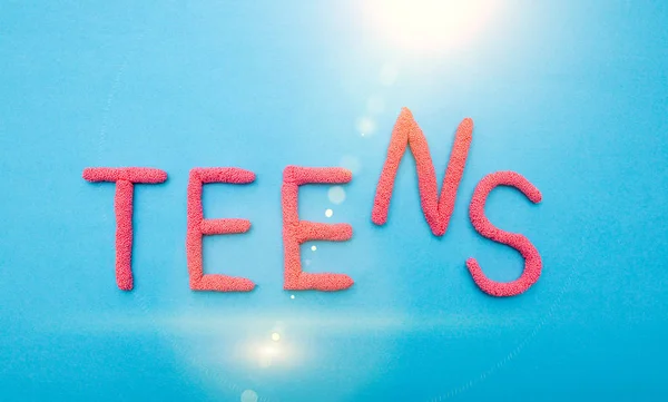 Слово підлітки в червоних літерах на синьому фоні з сонячним світлом, напис — стокове фото