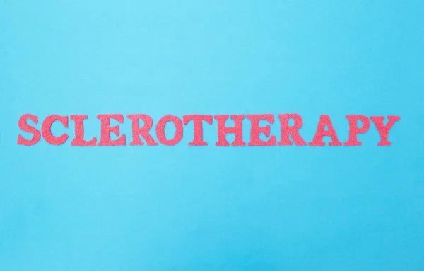 La palabra escleroterapia hecha de letras rojas sobre un fondo azul. El concepto de un procedimiento médico moderno para el tratamiento de las venas varicosas de las extremidades inferiores y hemorroides —  Fotos de Stock