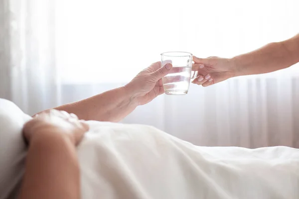 Une aide soignante tend une tasse d'eau à une femme âgée. Le concept de prise en charge des personnes âgées et de réhabilitation dans une pension, close-up, espace de copie — Photo