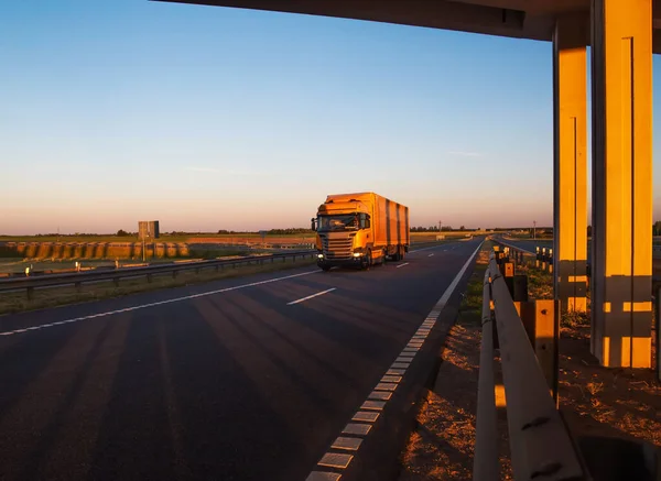 Un tren de carretera amarillo lleva carga contra el telón de fondo de una puesta de sol soleada y el cielo azul. Concepto de trabajo como camionero en una cadencia, antecedentes —  Fotos de Stock