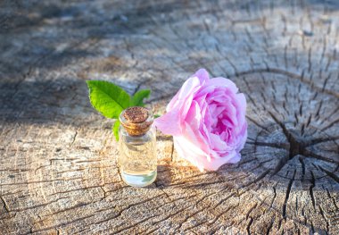 Ahşap bir arka planda gül kokusu olan bir şişe parfüm. Lezzetli çiçek aroması konsepti, aromaterapi.