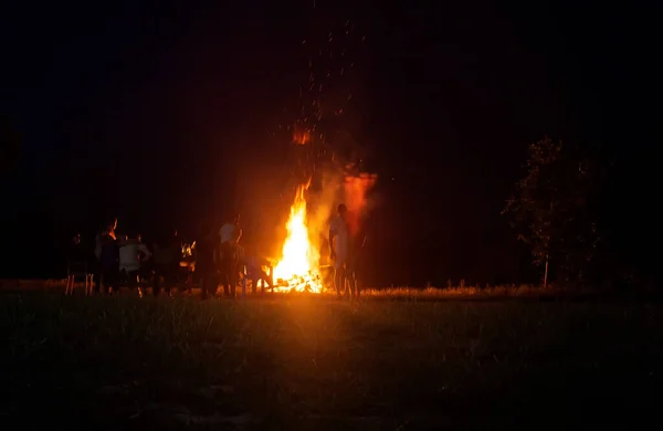Ludzie zrelaksować się na wakacjach w lesie w pobliżu dużego ogniska w nocy. Narodowe tło świąteczne, przestrzeń do kopiowania — Zdjęcie stockowe