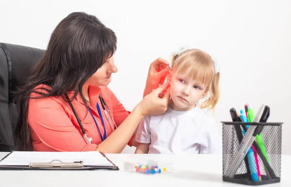 Cauacsian doctor otolaryngologist examines the ear of a little girl who has pain in her ear. The concept of otitis media and inflammation of the eardrum — Stock Photo, Image
