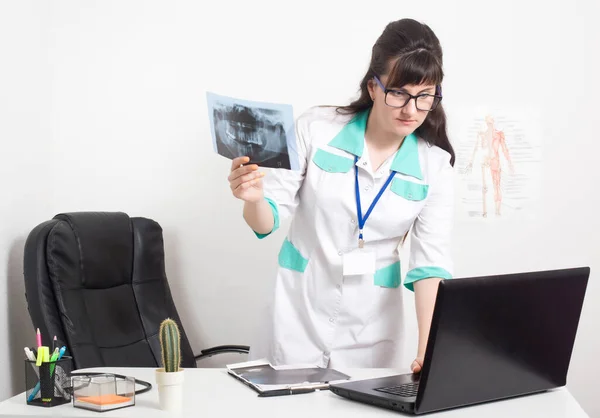 El radiólogo médico sostiene una imagen de rayos X de la mandíbula dental y comprueba los datos en una computadora portátil, consultorio médico en la clínica. Diagnósticos de radiación con rayos X, diagnóstico — Foto de Stock