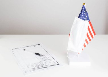 Coronavirus salgını sırasında Birleşik Devletler 'de başkanlık seçimi COVID 19. Koruyucu tıbbi maske ABD bayrağına asıldı. Kağıt oy pusulası masada. Başkan adayları arasında seçim