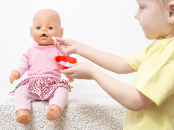 En liten flicka leker med en docka och behandlar henne med piller. Koncept för pediatrisk medicin och läkemedelsbehandling — Stockfoto