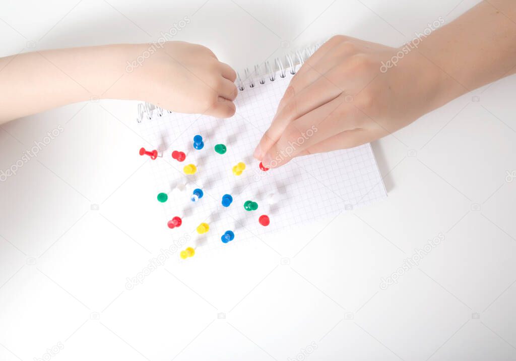 The hand of a child and a doctor sets multi-colored pins in a leaf on a white background. Autism development concept of a child thinking in games, autism, neurosonography