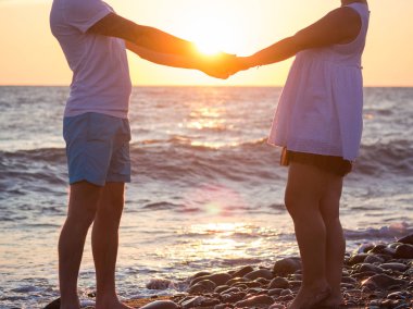 Genç çift gün batımında sahilde elele