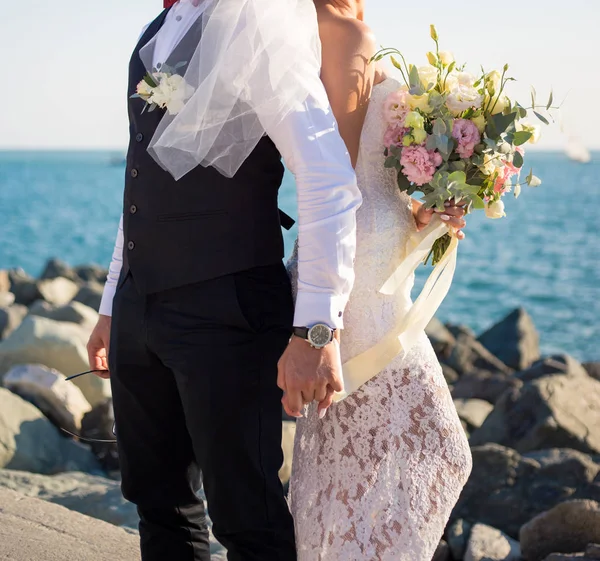 Newlyweds back to back with a bouquet near the sea