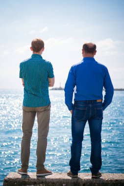 Erkekler denizin yanında durur.