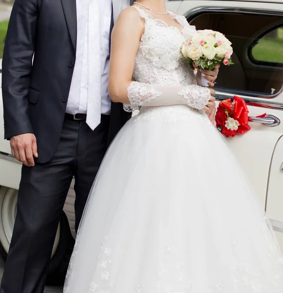 新娘和新郎拿着花束站在婚礼车旁边 — 图库照片