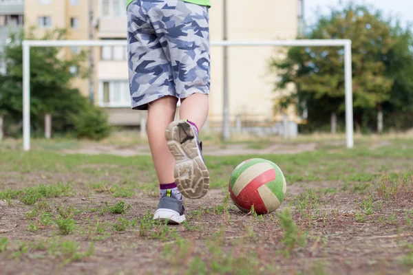 The child plays football on the school soccer field. The child trains to score the ball into the goal