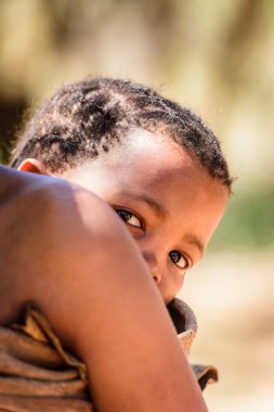 East Of Windhoek, Namibya - 3 Ocak 2016: Annesinin sırtında tanımlanamayan bushman bebeği. Bushman halkı Güney Afrika'nın yerli avcı-toplayıcı insanlarının üyeleridir.