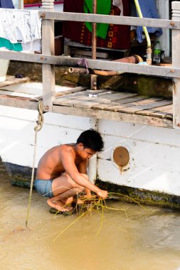 Mandalay, Myanmar - 26 Ağustos 2016: Tanımlanamayan Birmanyalı çocuk tekne motorunu çimlerden temizliyor. Myanma halkının yüzde 68'i Bamar etnik grubuna mensandı