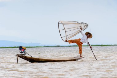 Inle Lake, Myanmar - 30 Ağustos 2016: Tanımlanamayan Birmanyalı balıkçı, özel el yapımı ağı olan bir teknede komik bir duruş sergiliyor. Bu Myanmar balıkçılık geleneksel yoludur