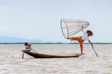 Inle Lake, Myanmar - 30 Ağustos 2016: Tanımlanamayan Birmanyalı balıkçı, özel el yapımı ağı olan bir teknede komik bir duruş sergiliyor. Bu Myanmar balıkçılık geleneksel yoludur