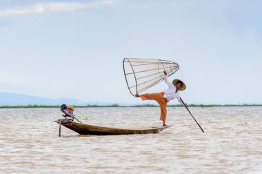 Inle Lake, Myanmar - 30 Ağustos 2016: Tanımlanamayan Birmanyalı balıkçı, özel el yapımı ağı olan bir teknede komik bir duruş sergiliyor. Bu Myanmar balıkçılık geleneksel yoludur