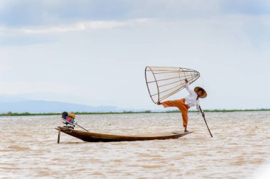 Inle Lake, Myanmar - 30 Ağustos 2016: Tanımlanamayan Birmanyalı balıkçı, özel el yapımı ağı olan bir teknede komik bir duruş sergiliyor. Bu Myanmar balıkçılık geleneksel yoludur