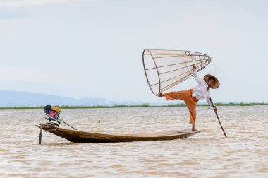 Inle Lake, Myanmar - 30 Ağustos 2016: Tanımlanamayan Birmanyalı balıkçı, özel el yapımı ağı olan bir teknede komik bir duruş sergiliyor. Bu Myanmar balıkçılık geleneksel yoludur