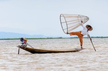 Inle Lake, Myanmar - 30 Ağustos 2016: Tanımlanamayan Birmanyalı balıkçı, özel el yapımı ağı olan bir teknede komik bir duruş sergiliyor. Bu Myanmar balıkçılık geleneksel yoludur