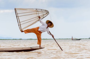 Inle Lake, Myanmar - 30 Ağustos 2016: Tanımlanamayan Birmanyalı balıkçı, özel el yapımı ağı olan bir teknede komik bir duruş sergiliyor. Bu Myanmar balıkçılık geleneksel yoludur
