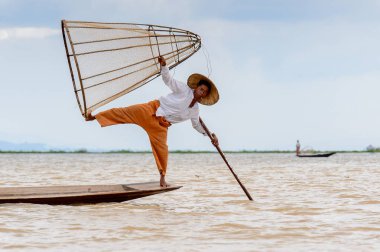 Inle Lake, Myanmar - 30 Ağustos 2016: Tanımlanamayan Birmanyalı balıkçı, özel el yapımı ağı olan bir teknede komik bir duruş sergiliyor. Bu Myanmar balıkçılık geleneksel yoludur