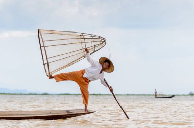 Inle Lake, Myanmar - 30 Ağustos 2016: Tanımlanamayan Birmanyalı balıkçı, özel el yapımı ağı olan bir teknede komik bir duruş sergiliyor. Bu Myanmar balıkçılık geleneksel yoludur