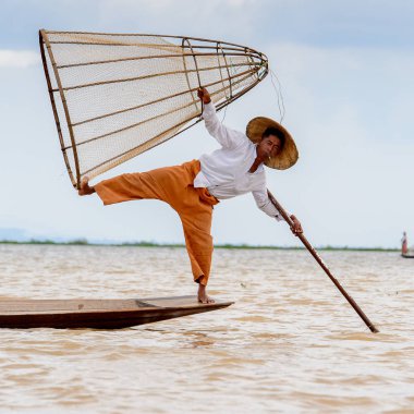Inle Lake, Myanmar - 30 Ağustos 2016: Tanımlanamayan Birmanyalı balıkçı, özel el yapımı ağı olan bir teknede komik bir duruş sergiliyor. Bu Myanmar balıkçılık geleneksel yoludur