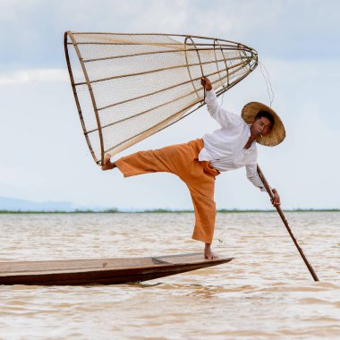 Inle Lake, Myanmar - 30 Ağustos 2016: Tanımlanamayan Birmanyalı balıkçı, özel el yapımı ağı olan bir teknede komik bir duruş sergiliyor. Bu Myanmar balıkçılık geleneksel yoludur